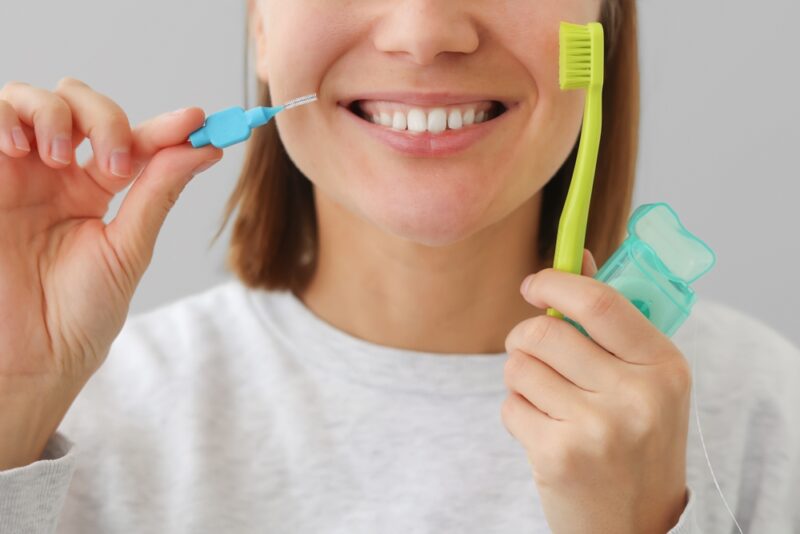 Osoba drži interdentalnu četkicu, četkicu za zube i zubni konac kao deo pravilne svakodnevne nege desni i međuzubnog prostora